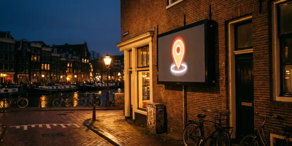 Digitaal billboard met locatiepinpictogram op bakstenen gevel langs Amsterdamse gracht in de Jordaan, verlicht door gouden avondlicht.