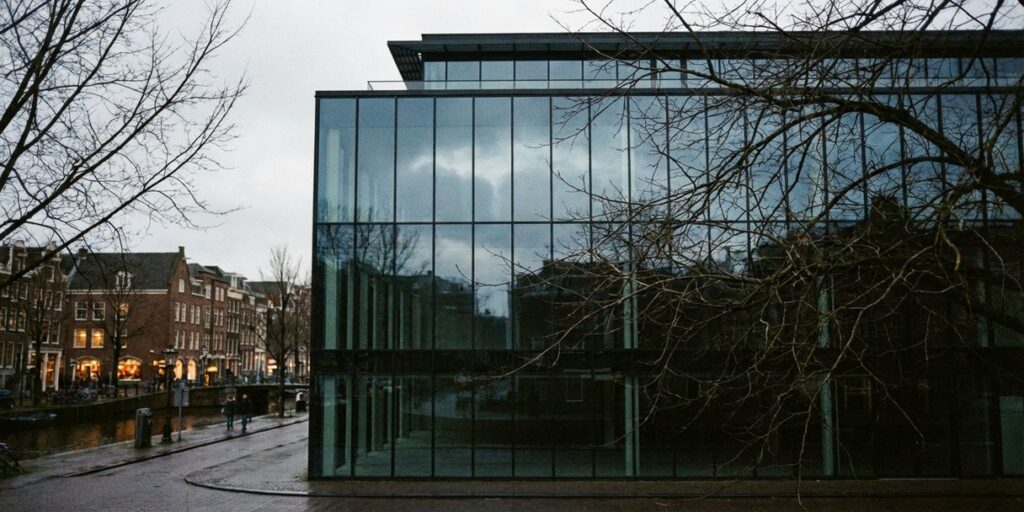 Leeg modern kantoorgebouw met glazen gevel langs Amsterdamse gracht, donker binnen terwijl omliggende gebouwen verlicht zijn